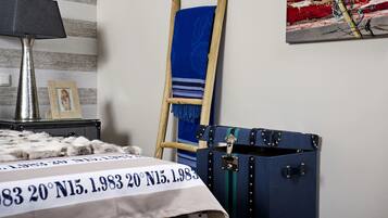Une pièce avec un lit, une échelle en bois, une valise bleue et une lampe.