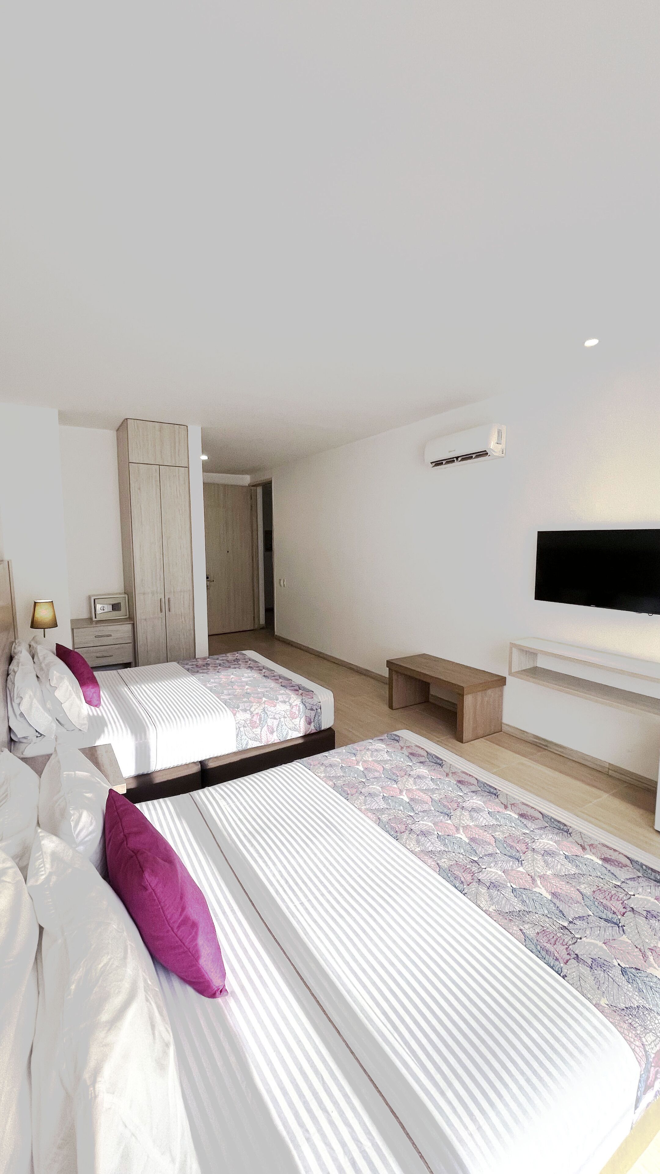 A modern bedroom with two beds, a TV, and a wardrobe.