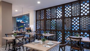 A restaurant with wooden tables and chairs, a decorative partition with circular cutouts, and a view of trees outside. - MS Pacífico Chipichape Plus (Cali)