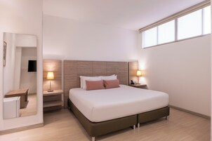 A modern hotel room with a large bed, bedside lamps, a nightstand, and a mirror.