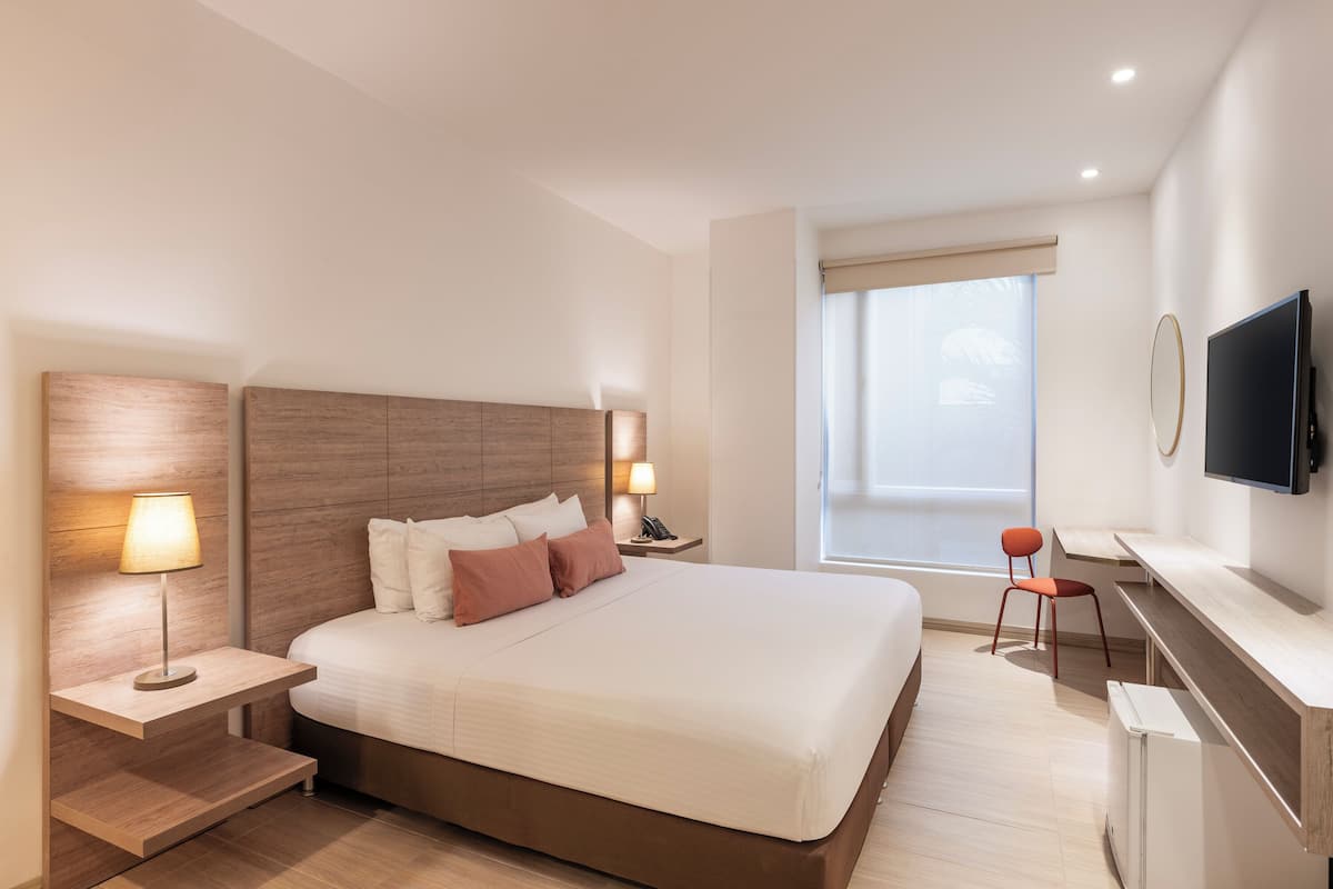 A modern hotel room with a large bed, bedside lamps, a desk with a chair, a television, and a window with a view.
