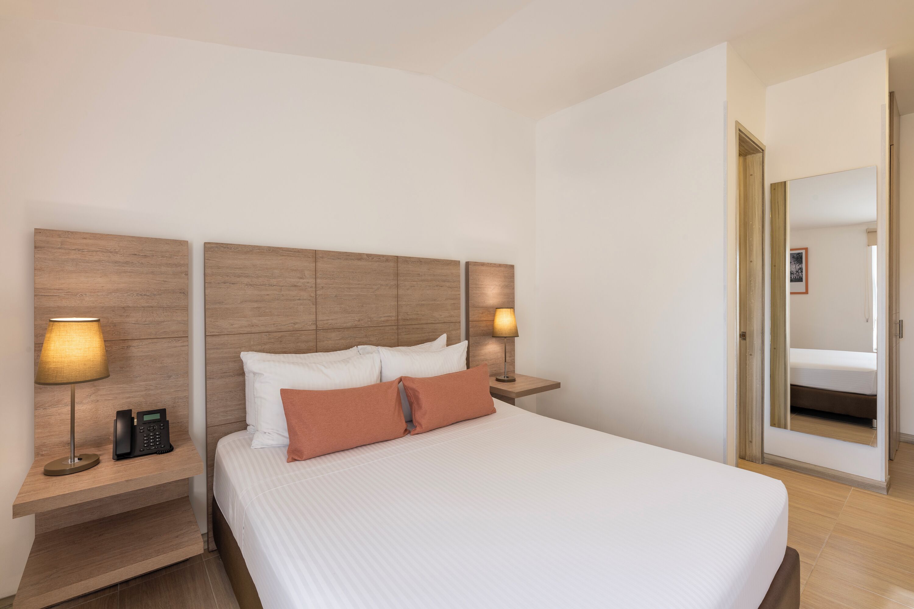 A hotel room with a large bed, two bedside tables with lamps, a telephone, and a mirror on the wall.