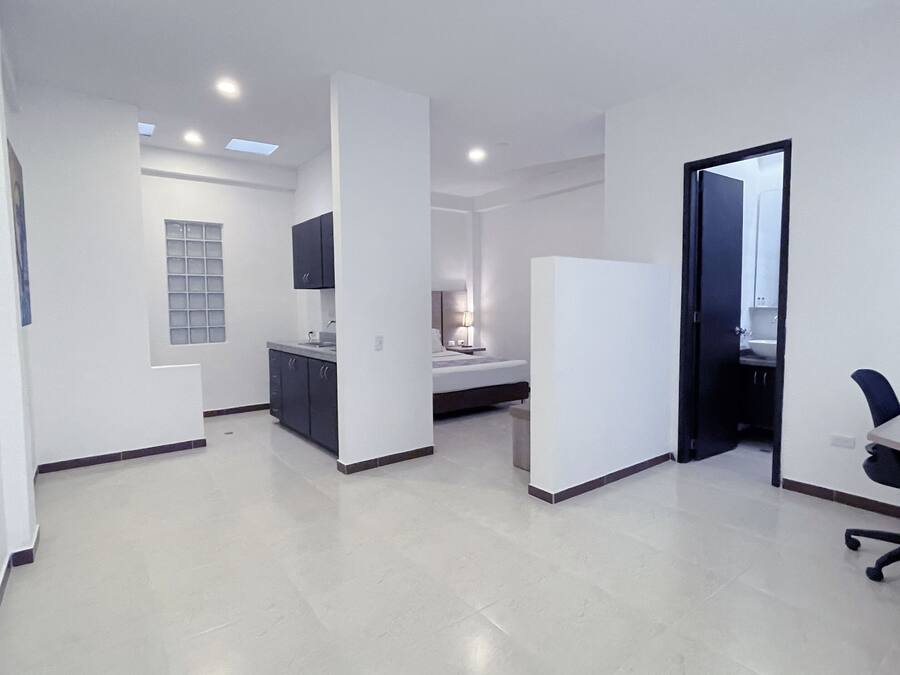 Quarto moderno e bem iluminado, com cama, mesa de cabeceira e um pequeno espaço para escritório.