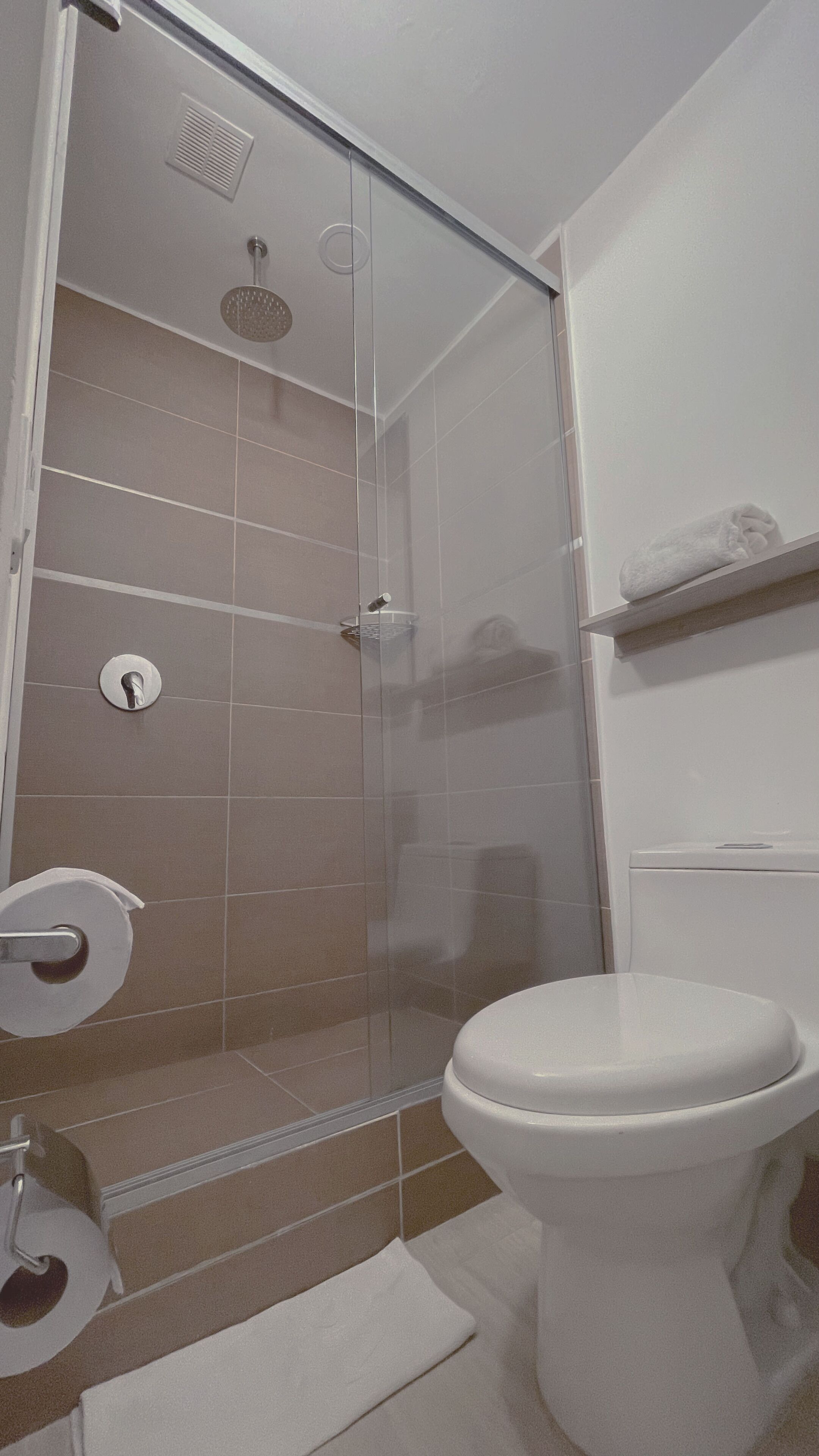 Un baño con cabina de ducha de vidrio, inodoro y barra para toallas.