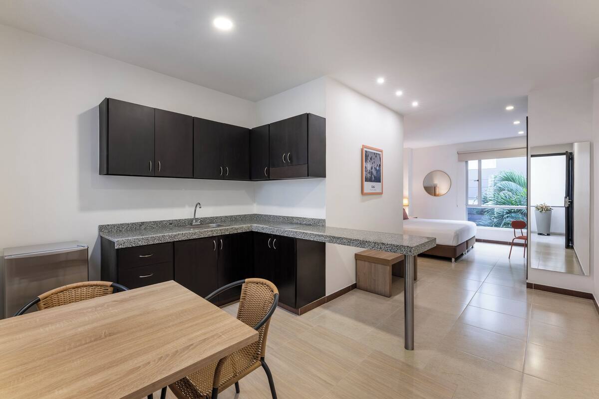 A modern kitchen with dark cabinets, a granite countertop, and a dining area with a wooden table and wicker chairs.