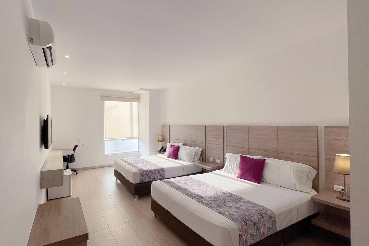 A hotel room with two beds, a desk, a chair, a TV, and a window.