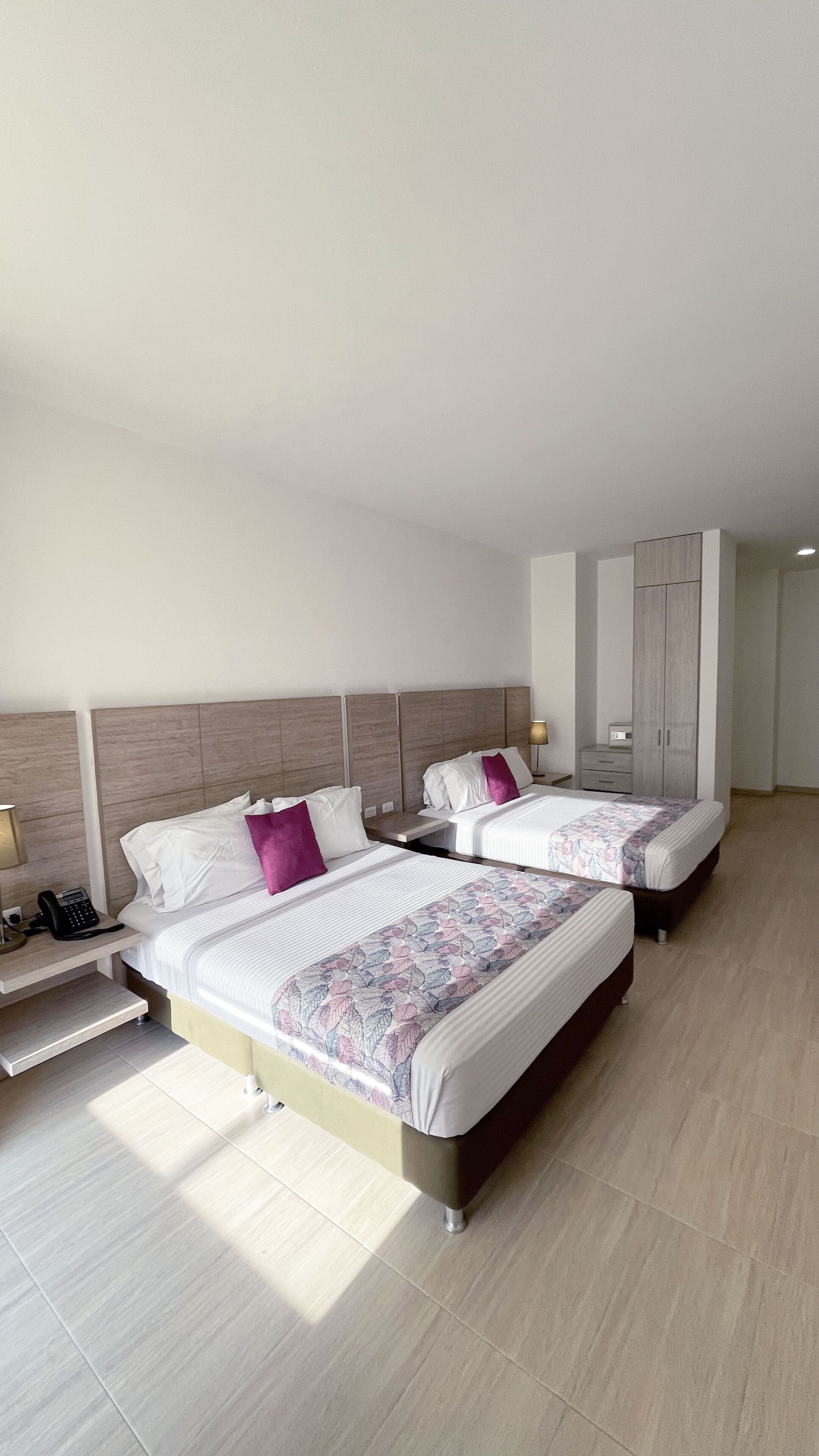 Una habitación de hotel moderna con dos camas, un armario, una mesita de noche con lámpara y un teléfono.