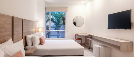 Una habitación de hotel moderna con una cama grande, un escritorio, un televisor y una ventana con vistas a palmeras.