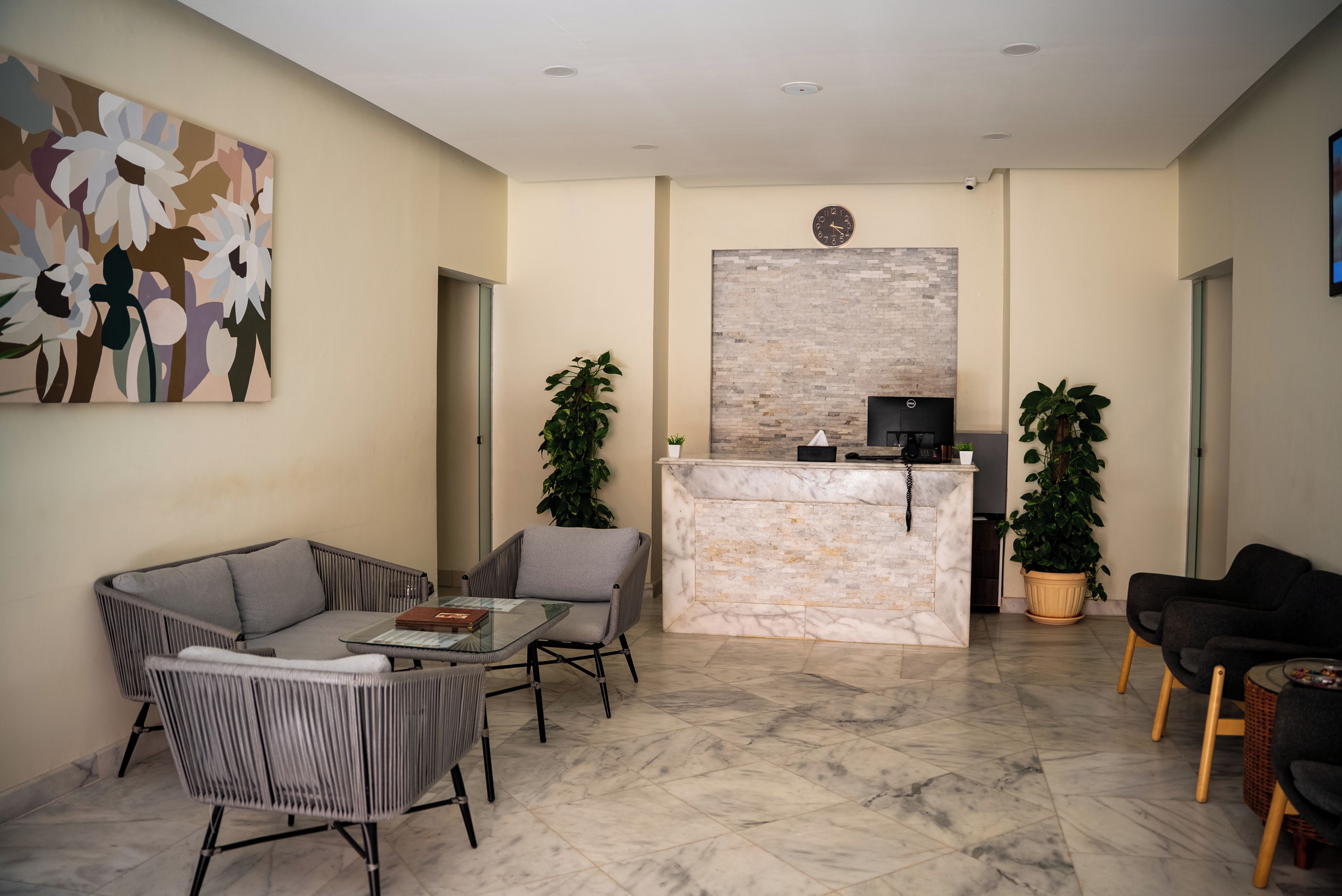 Un área de recepción con un mostrador de mármol, dos plantas en macetas, un sofá y una silla.