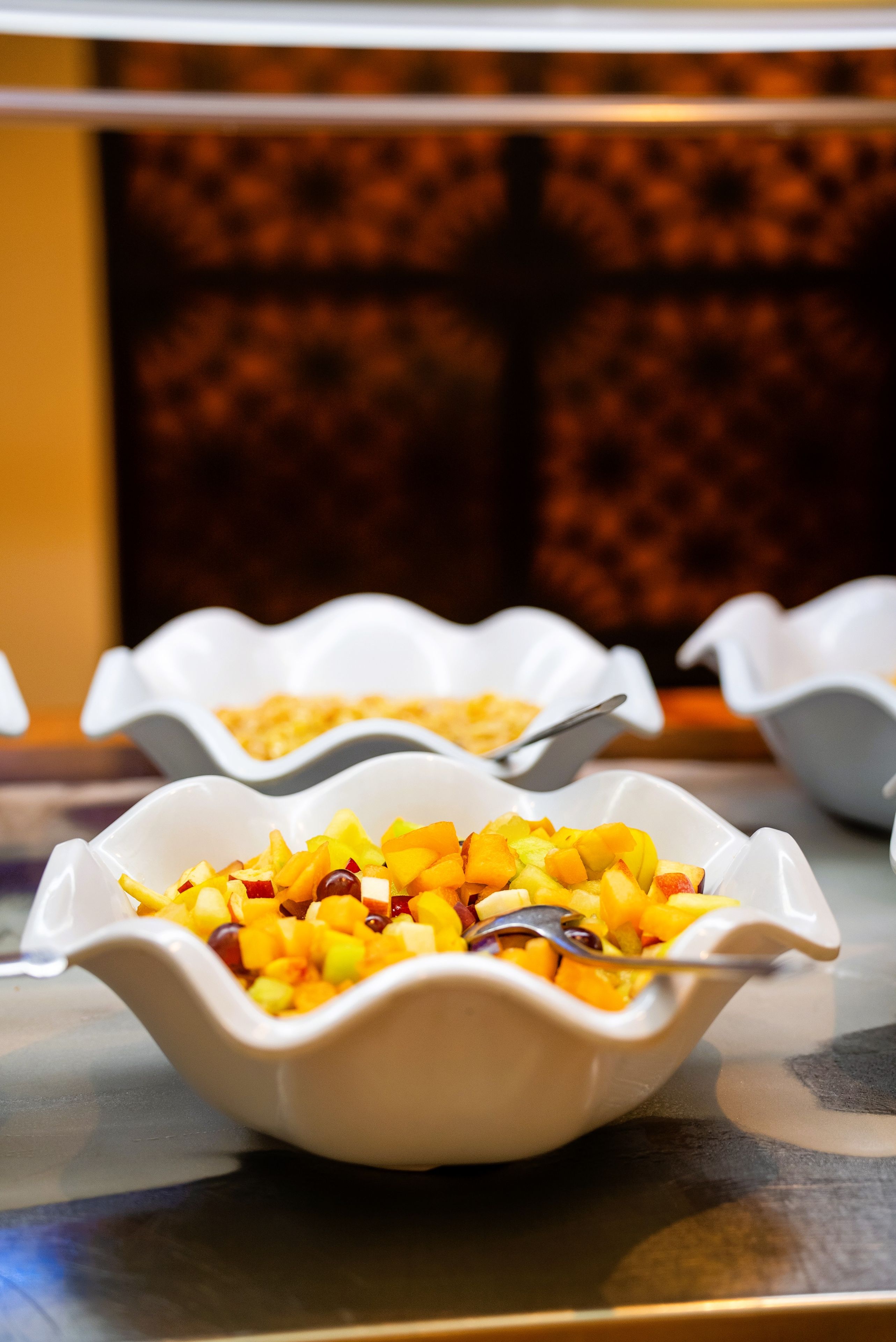 A buffet table with white bowls containing fruit salad.