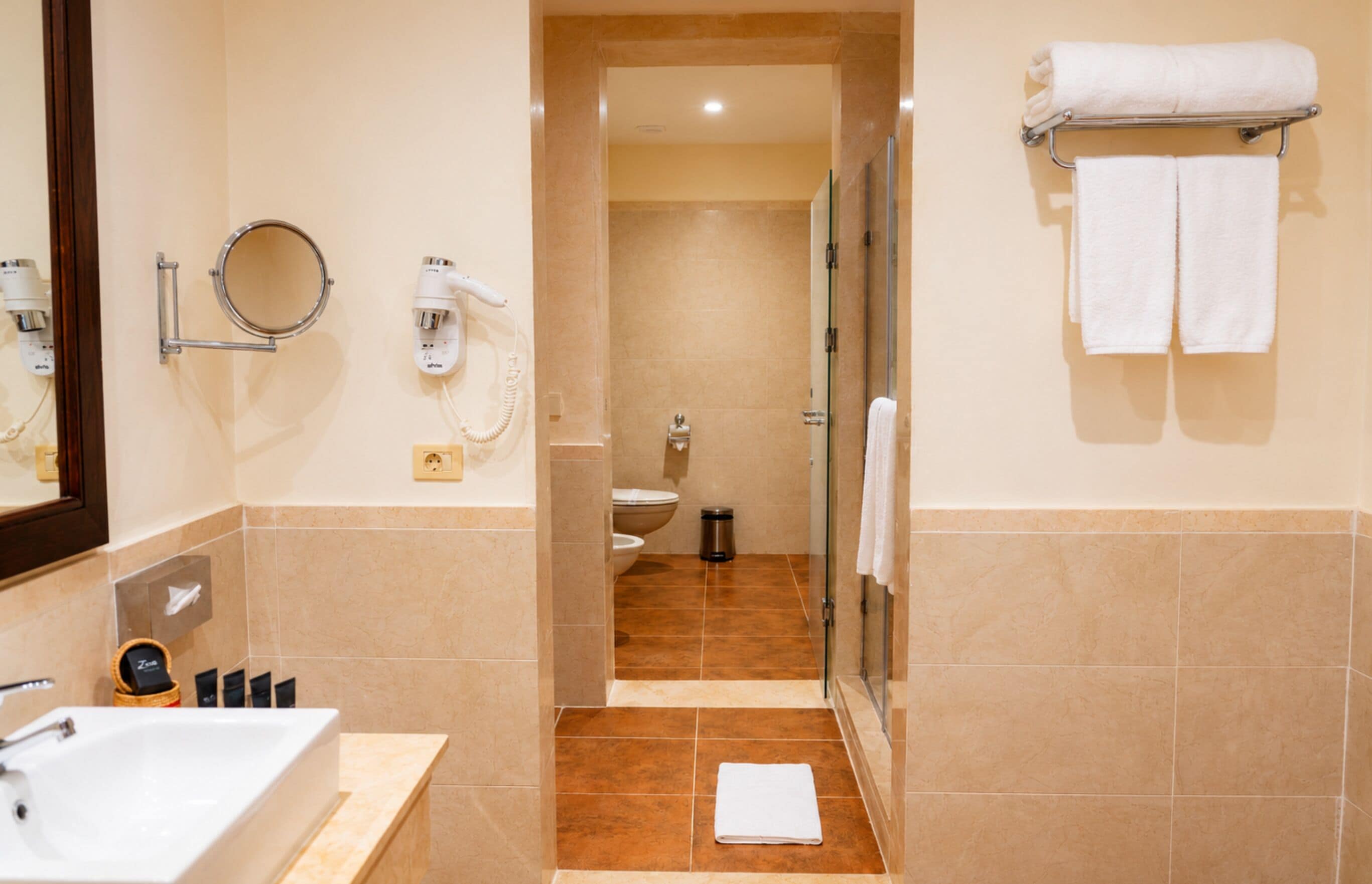 Une salle de bain d’hôtel équipée d’un lavabo, d’un miroir, d’un sèche-cheveux et d’un porte-serviettes.