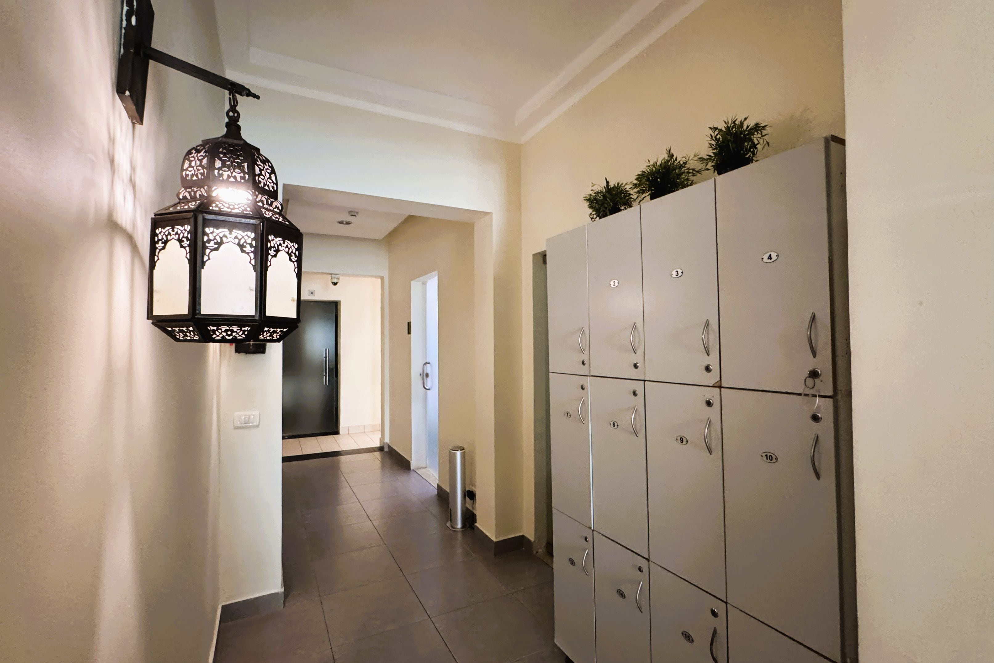 A hallway with lockers, a wall-mounted light fixture, and a door leading to another room.