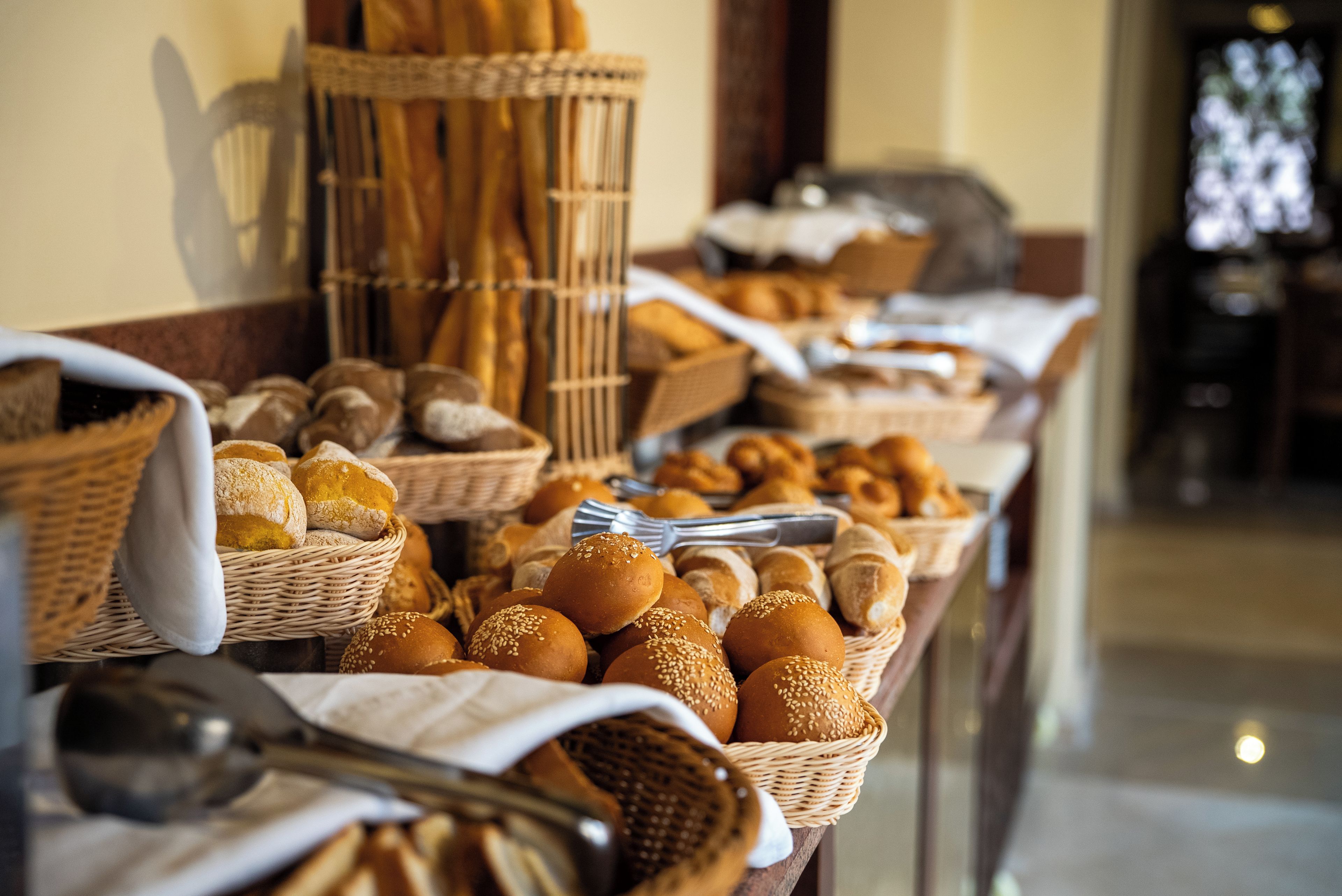 Ein Buffet mit verschiedenen Brotsorten und Gebäck, darunter Brötchen und Semmeln, präsentiert in Körben und auf einer mit Stoff bedeckten Tischdecke.