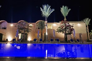A poolside area with lounge chairs and umbrellas, a building with arches, and palm trees. - Gemma Resort (Marsa Alam)