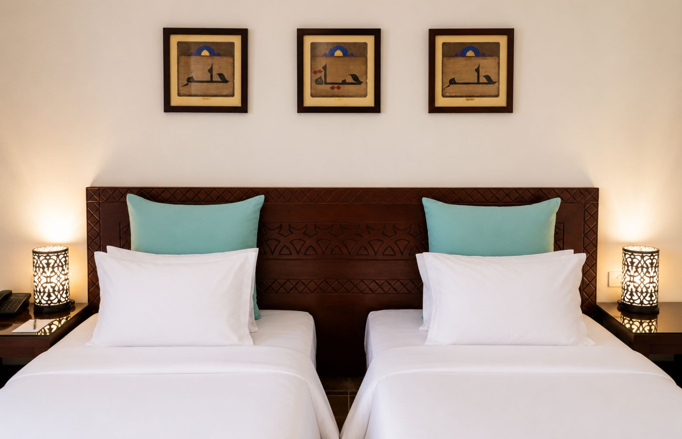 A hotel room with two beds, a patterned headboard, and three framed pictures on the wall.