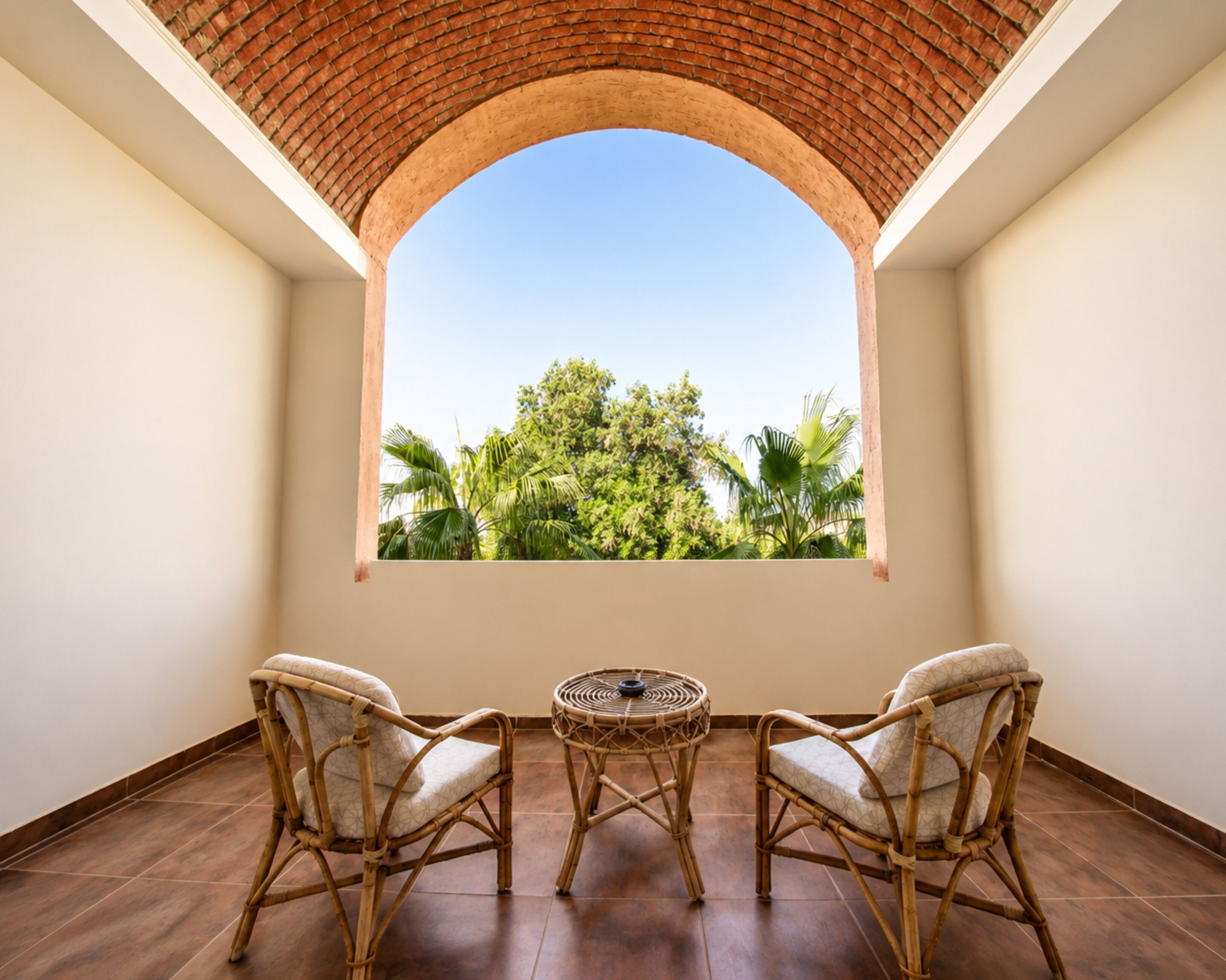 A balcony with two wicker chairs and a small round table, overlooking a lush green landscape.
