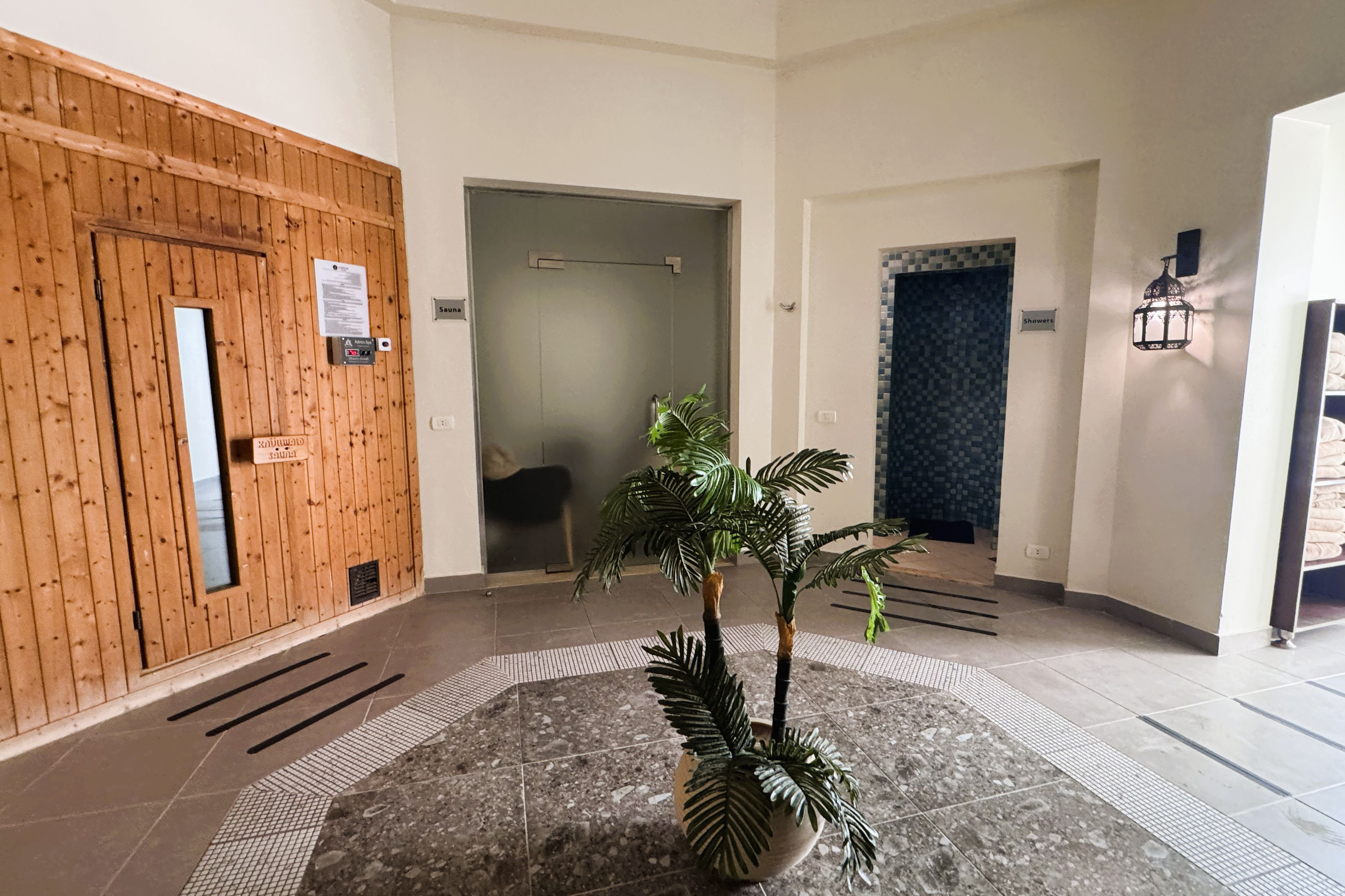A lobby with a wooden door, a sign indicating a sauna, a tiled floor, and a potted plant.