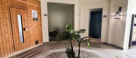 A lobby with a wooden door, a sign indicating a sauna, a tiled floor, and a potted plant.