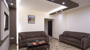 A modern living room with two sofas, a coffee table, and a cityscape painting on the wall. - Al-Riyati For Hotel Apartments (Aqaba)