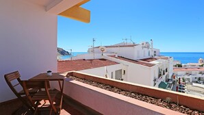 A balcony with a table and chairs, overlooking a coastal town with buildings and the sea. - A06 - Seaview 1 Bed Apartment by DreamAlgarve (Lagos)