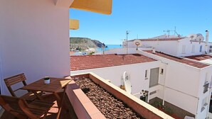 A balcony with a table and chairs, overlooking a coastal area with buildings and a cliff. - A06 - Seaview 1 Bed Apartment by DreamAlgarve (Lagos)