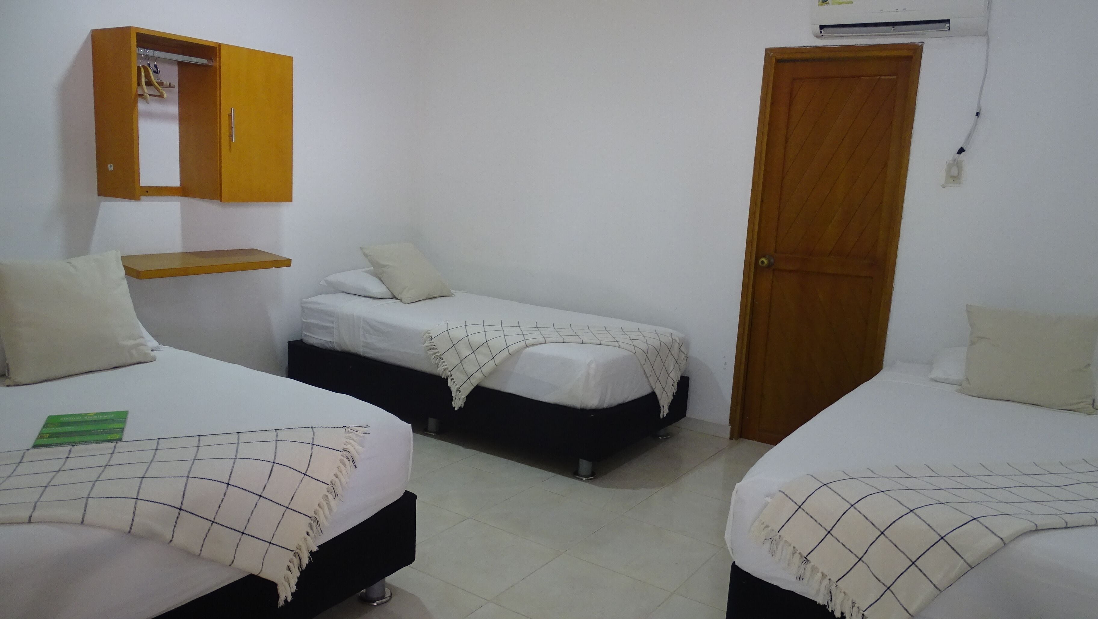 Una habitación con dos camas, un armario de madera, un estante pequeño y una puerta.