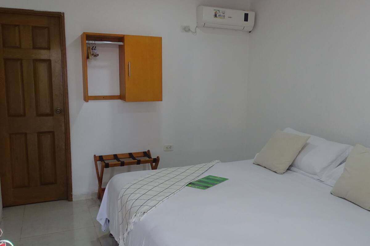 Une chambre à coucher comprenant un lit, une armoire en bois, un banc et un climatiseur fixé au mur.