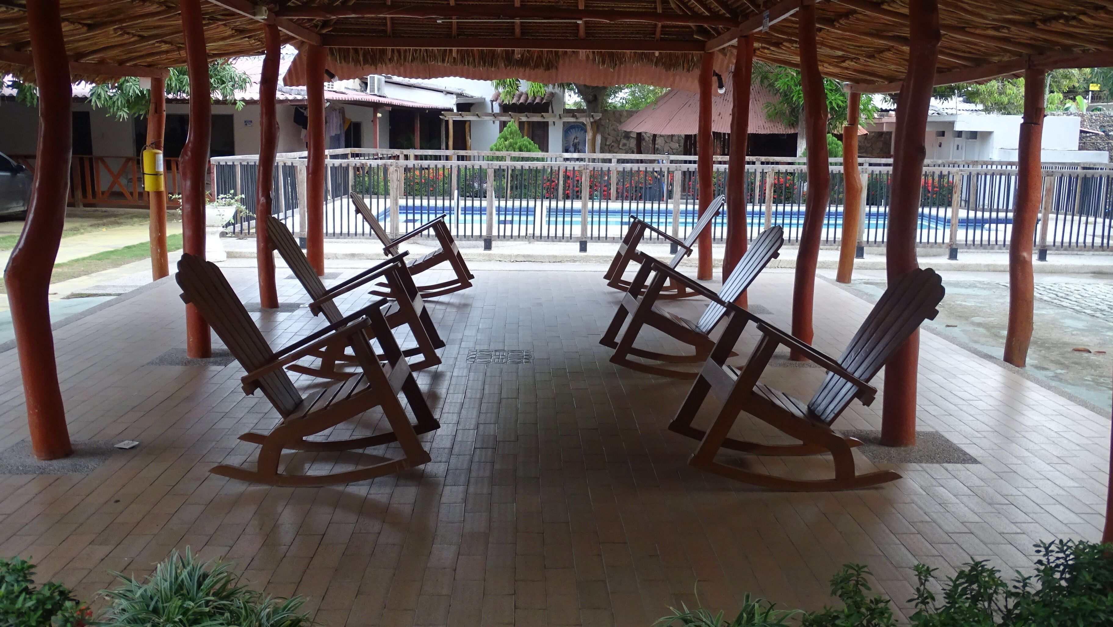 Un espacio de estar al aire libre techado con sillas de balancín de madera y piso de baldosas.