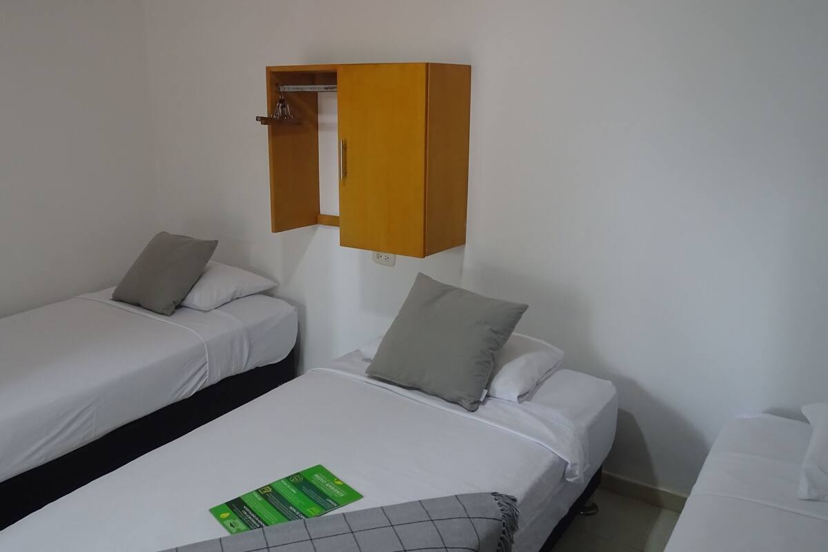 Une chambre d’hôtel avec deux lits simples, une armoire en bois et une carte d’information verte posée sur le lit.