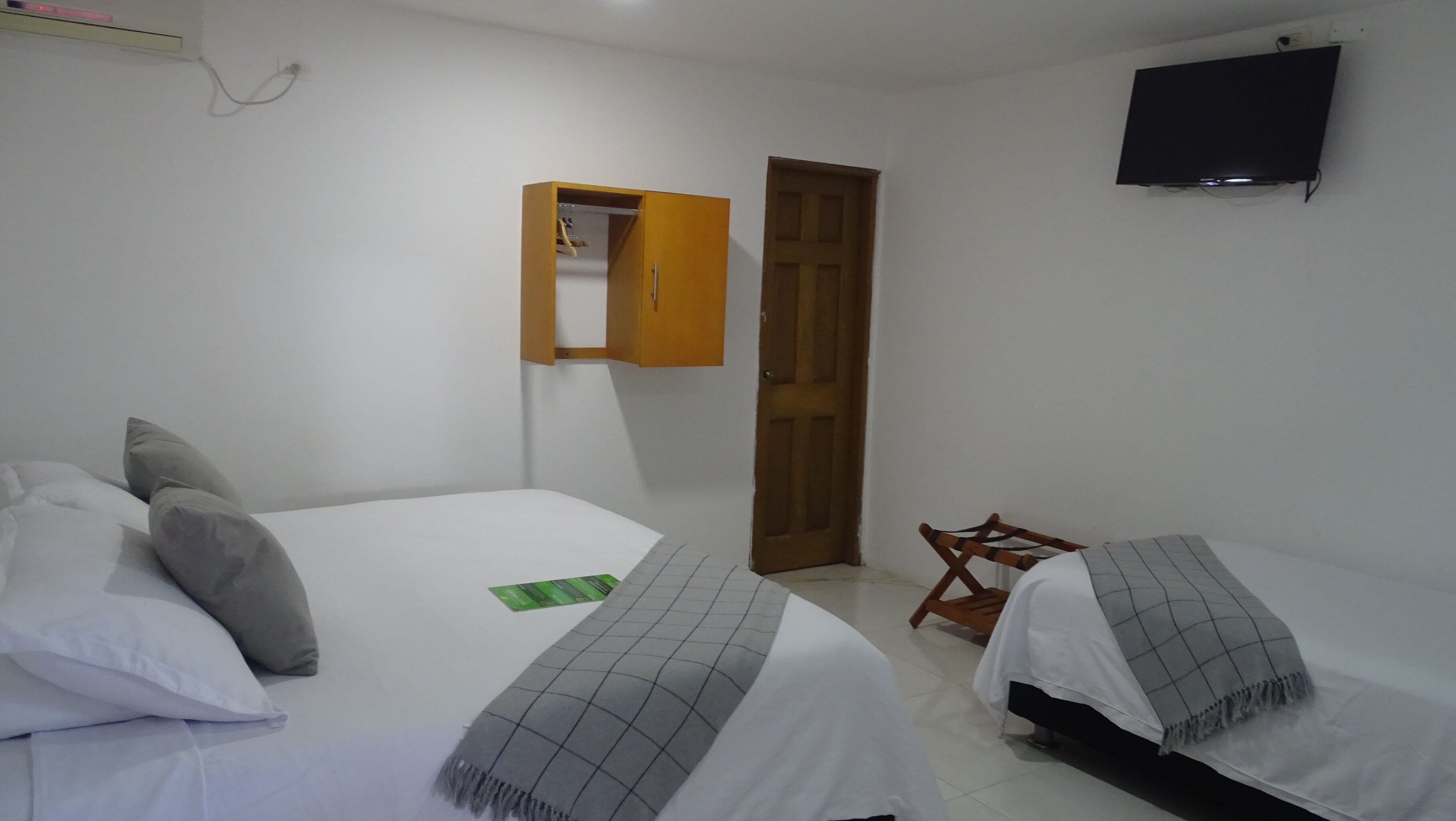 A bedroom with two beds, a wooden wardrobe, a television, and a door.