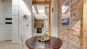 Un coin repas avec une table en bois, des chaises transparentes, un plateau décoratif et un mur en briques agrémenté d’une lucarne.