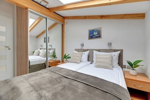 A bedroom with a bed, bedside tables, a nightstand, a potted plant, and a painting on the wall.