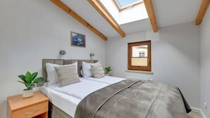 Une chambre avec un puits de lumière, un lit recouvert d’une couverture à motifs, une plante sur la table de chevet et une fenêtre.