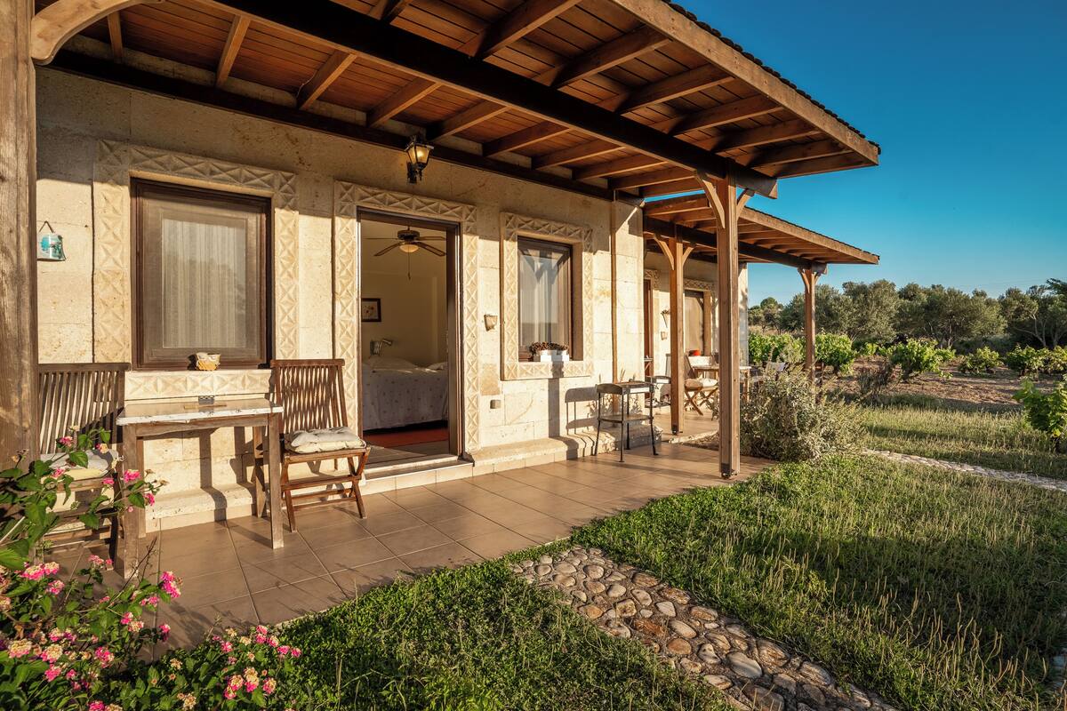 A covered patio with outdoor seating, a stone pathway, and a garden with flowers.