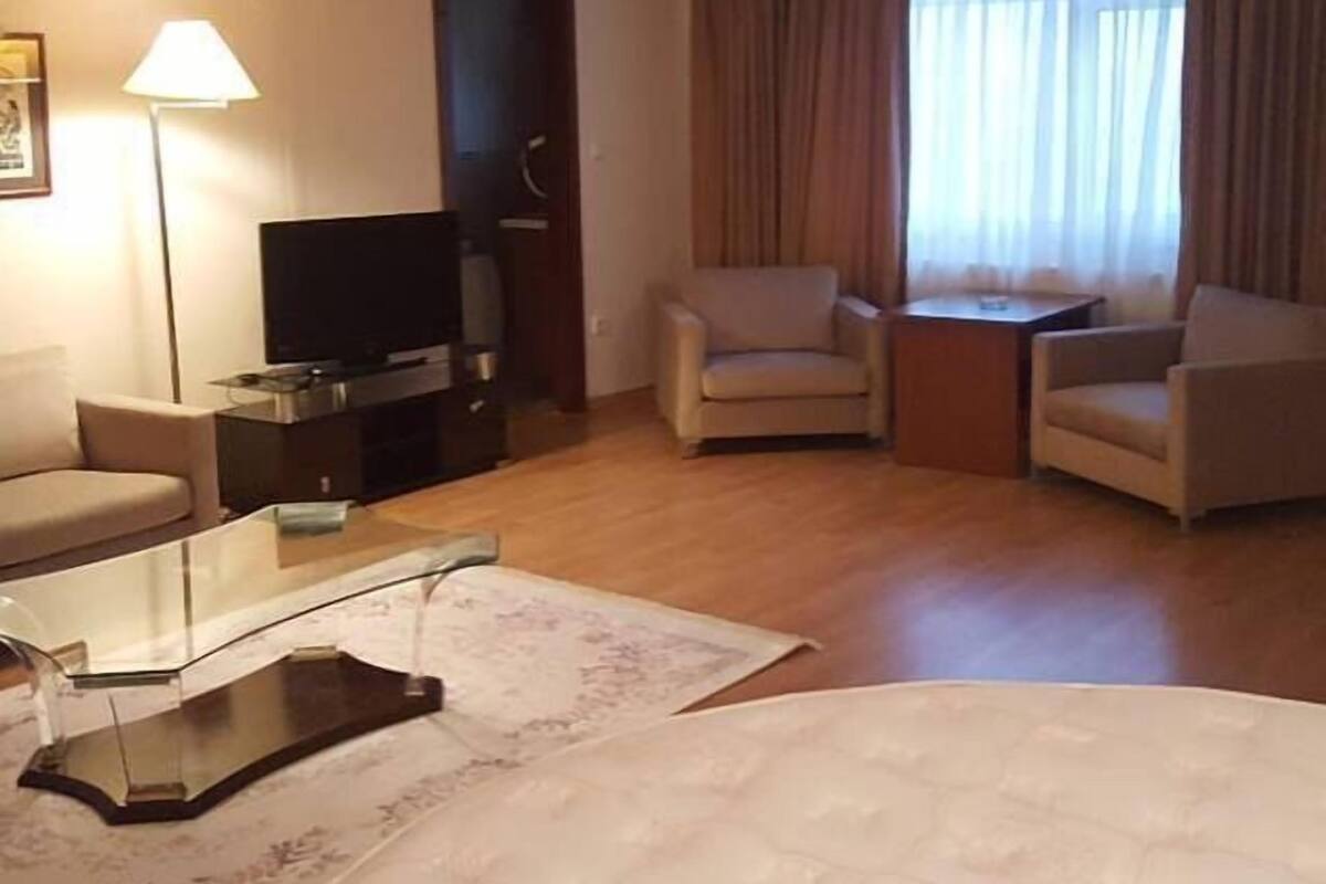 A hotel room with a sofa, armchair, TV, and a small table.