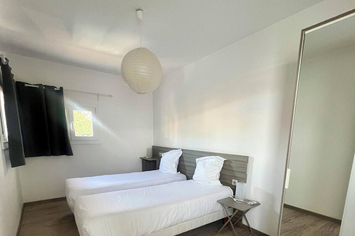 Un dormitorio con cama, mesita de noche, espejo y ventana con cortinas.