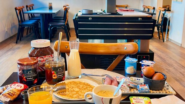 Ett frukostbricka med bakverk, bröd och drycker står på ett bord i en restaurang med modern inredning och stora fönster.