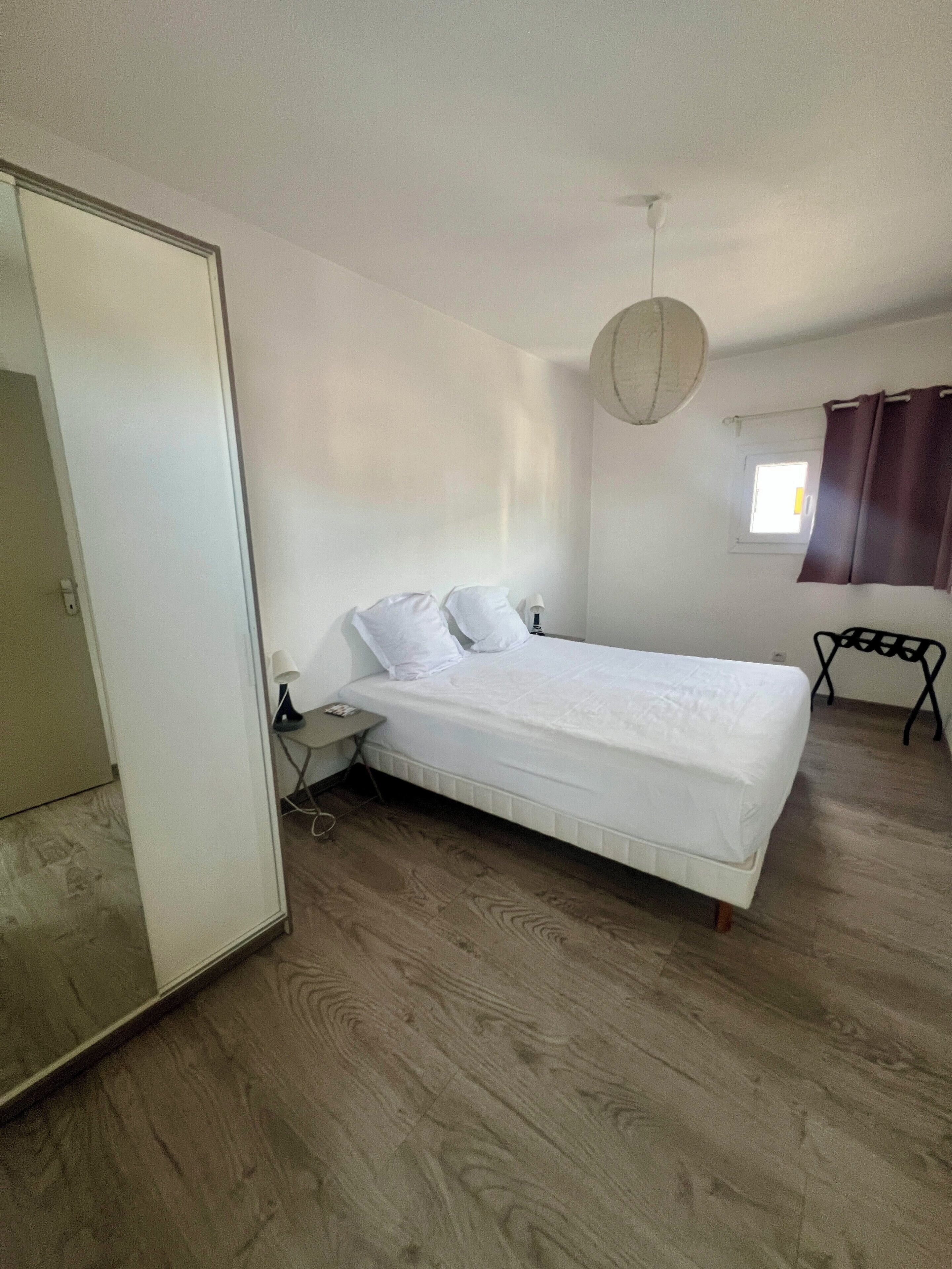 A bedroom with a bed, a bedside table, a lamp, a window with curtains, and a door.