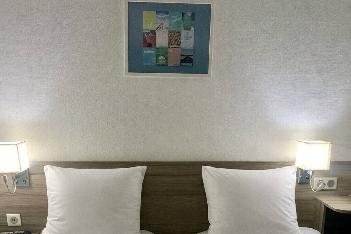 Una habitación de hotel con dos camas individuales, cabeceros, lámparas de noche y una obra de arte en la pared.