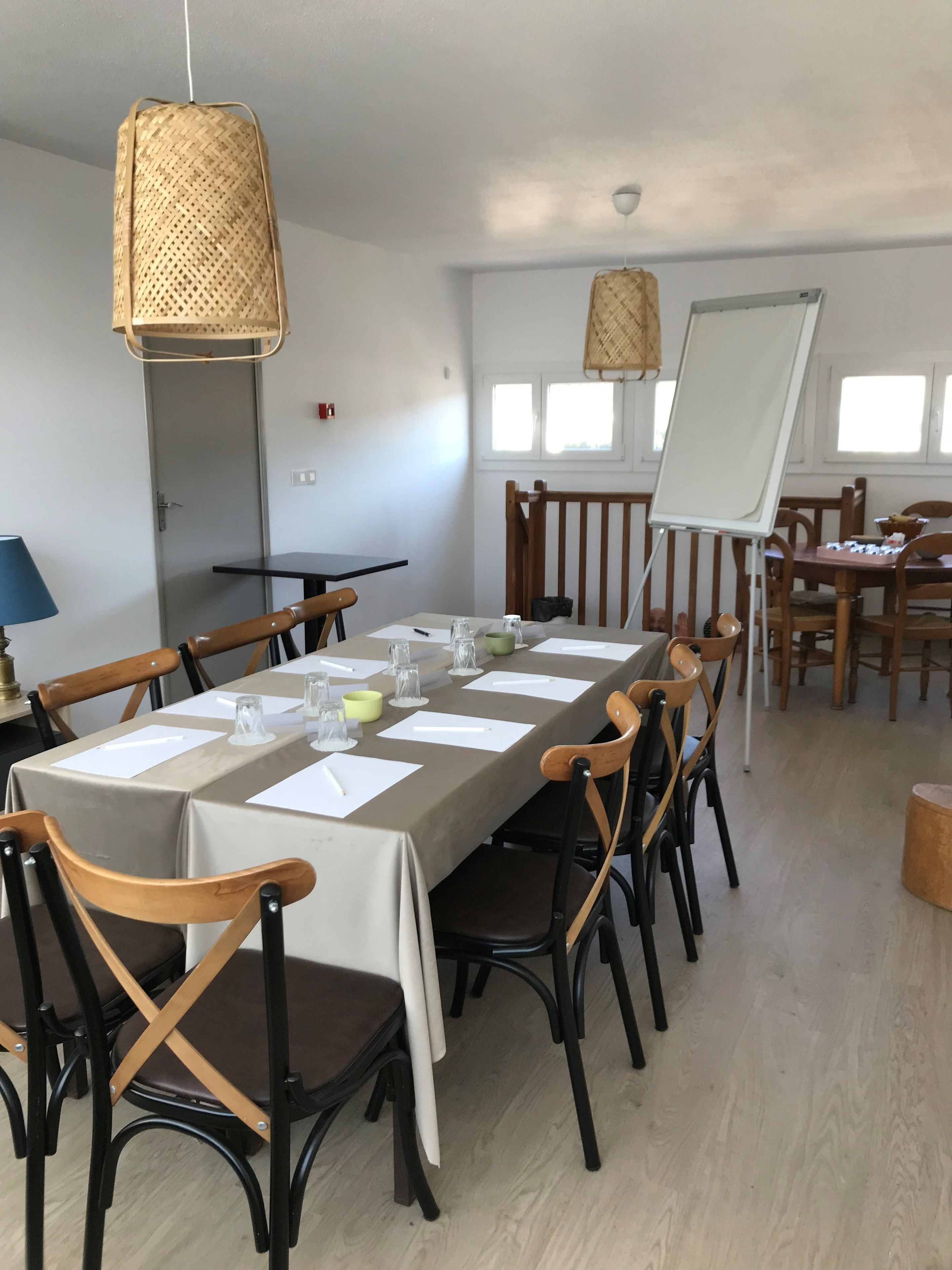 A conference room with a long table, chairs, a whiteboard, and hanging wicker lamps.