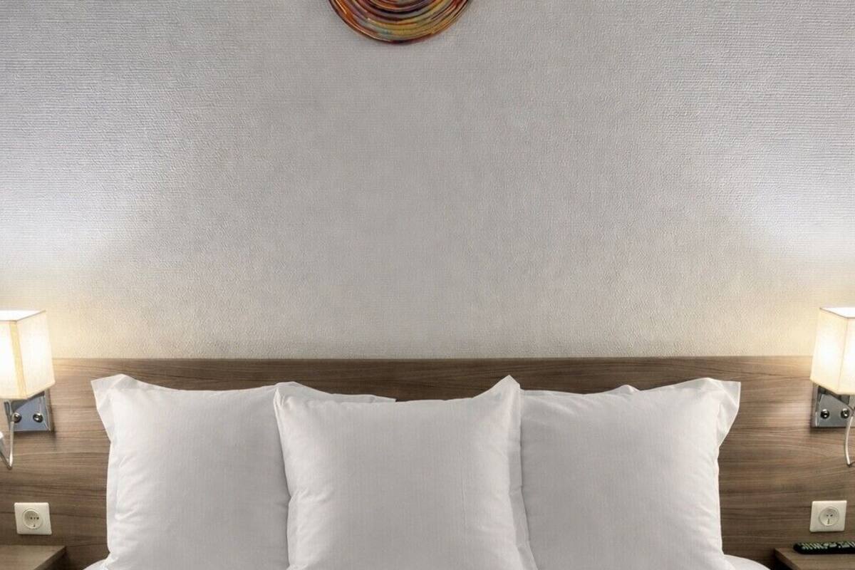 Una cama bien hecha con sábanas y almohadas blancas, cabecera de madera y dos lámparas de noche a cada lado.