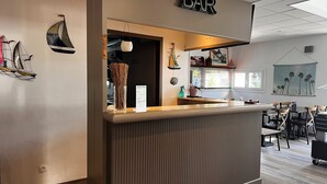 En bardisk med en träinredning, en skylt ovanför och utsikt över matsalen med bord och stolar.