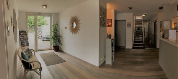 A hallway with a bench, a potted plant, a sunburst mirror, and a staircase leading to another room.