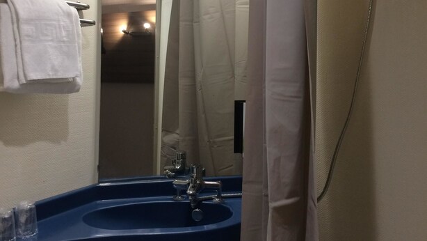 Une salle de bain avec un lavabo bleu, un miroir, un rideau de douche et un porte-serviettes.