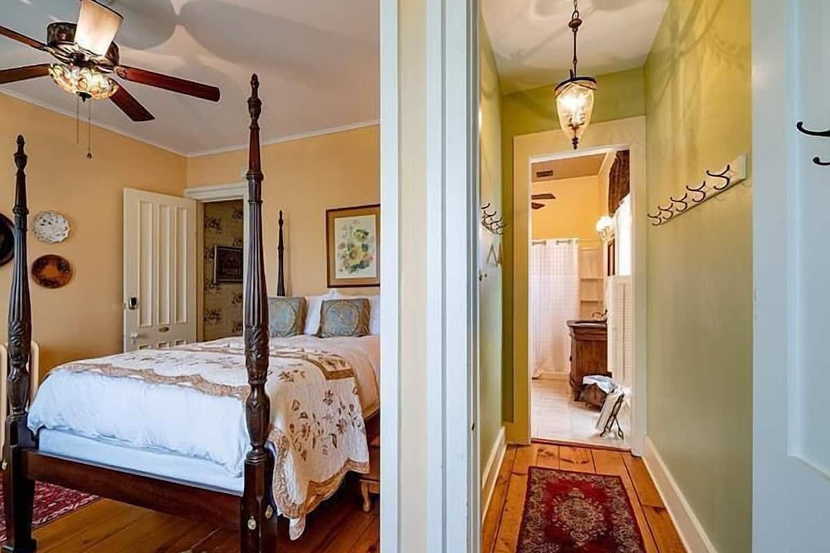 A bedroom with a four-poster bed, a ceiling fan, and a chandelier.