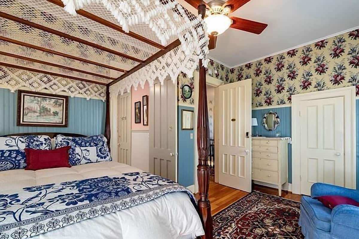 A bedroom with a four-poster bed, a ceiling fan, and floral wallpaper.