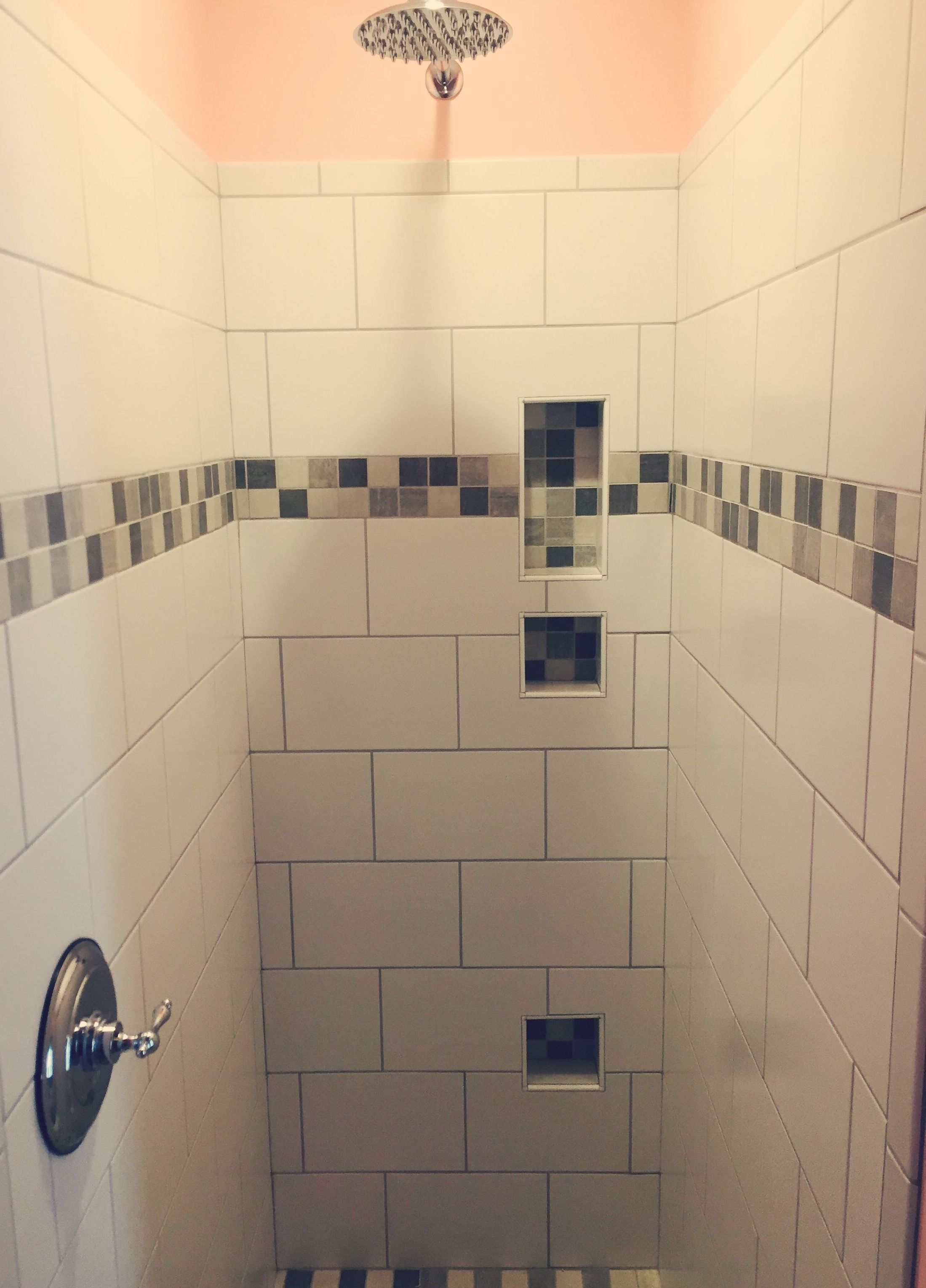 Ducha con azulejos blancos, una ventana pequeña y un cabezal de ducha.