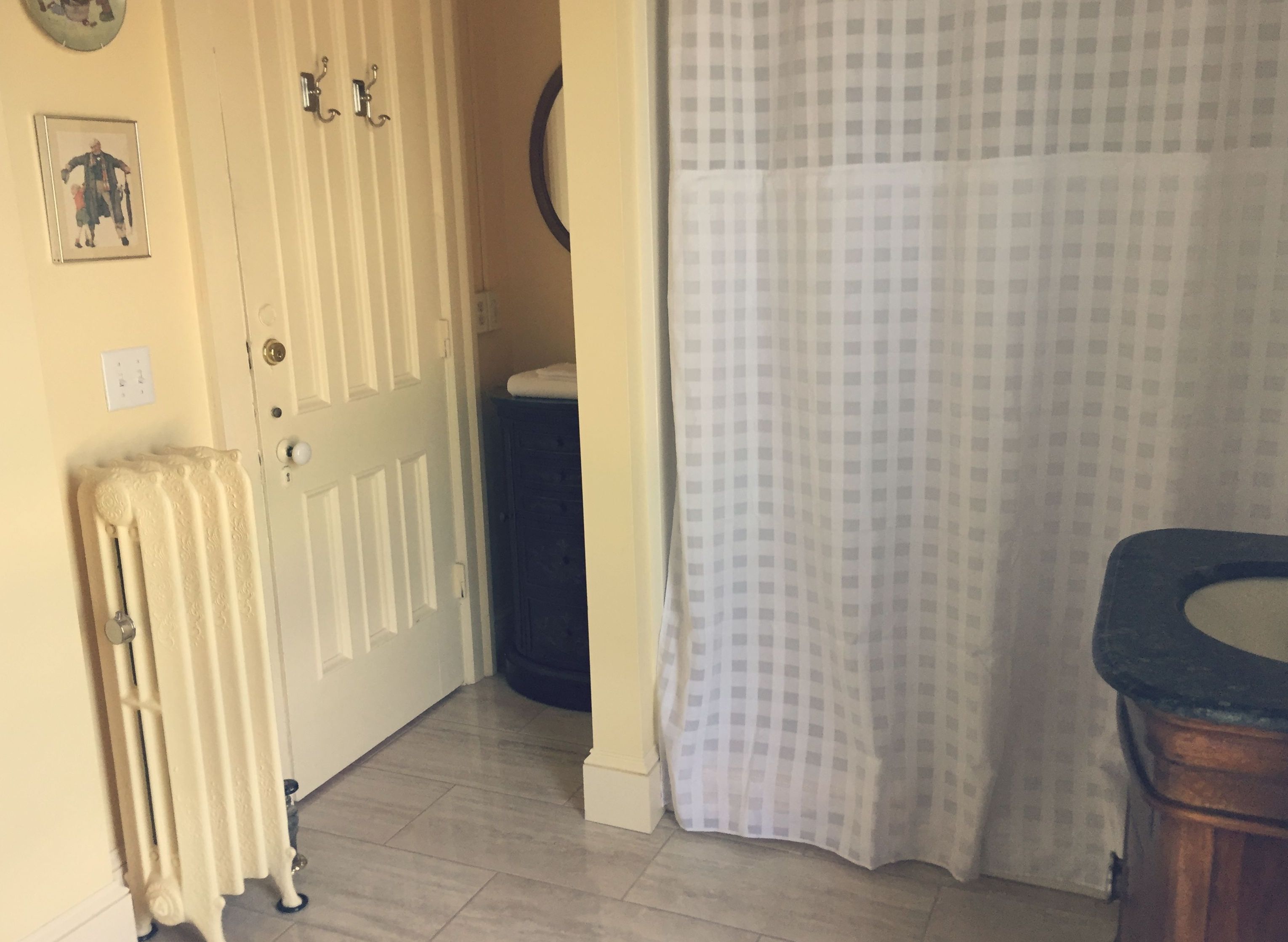 Un baño con un radiador blanco, una cortina de ducha a cuadros y un armario de madera.