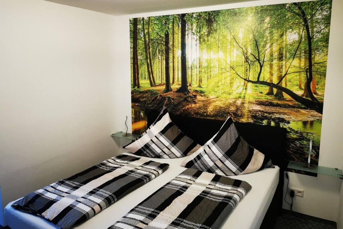 Un dormitorio con cama, mesita de noche y un gran mural temático de un bosque.
