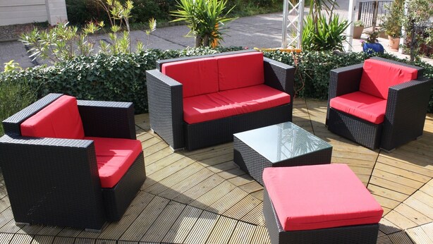 Un patio con muebles de mimbre y cojines rojos.